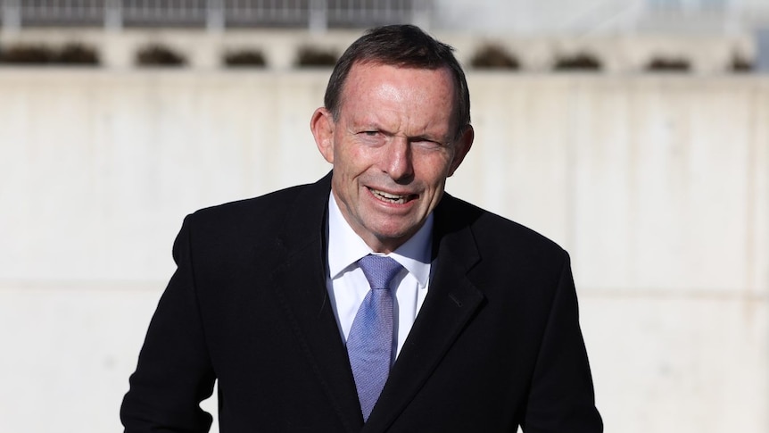 Tony Abbott arrives at Federal Parliament with bark blue suit, a white shirt, a like blue tie and a strained facial expression.