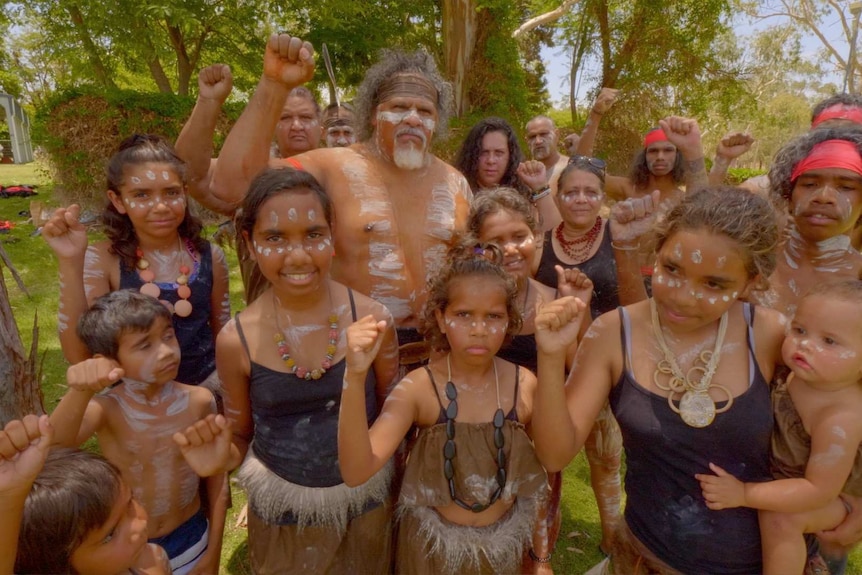 Wangan and Jagalingou people in ceremonial dress fist pumping at a traditional ceremony.