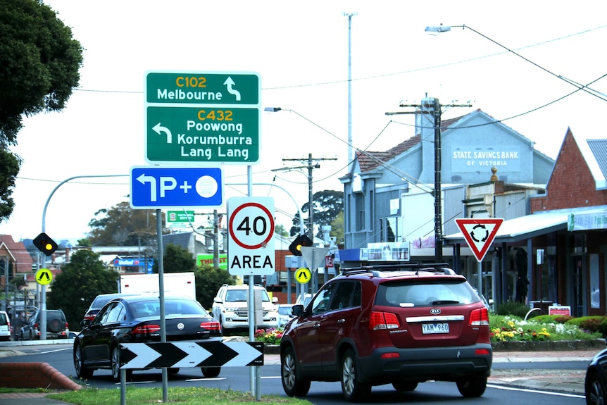 Cars drive through a roundabout underneath road signs.