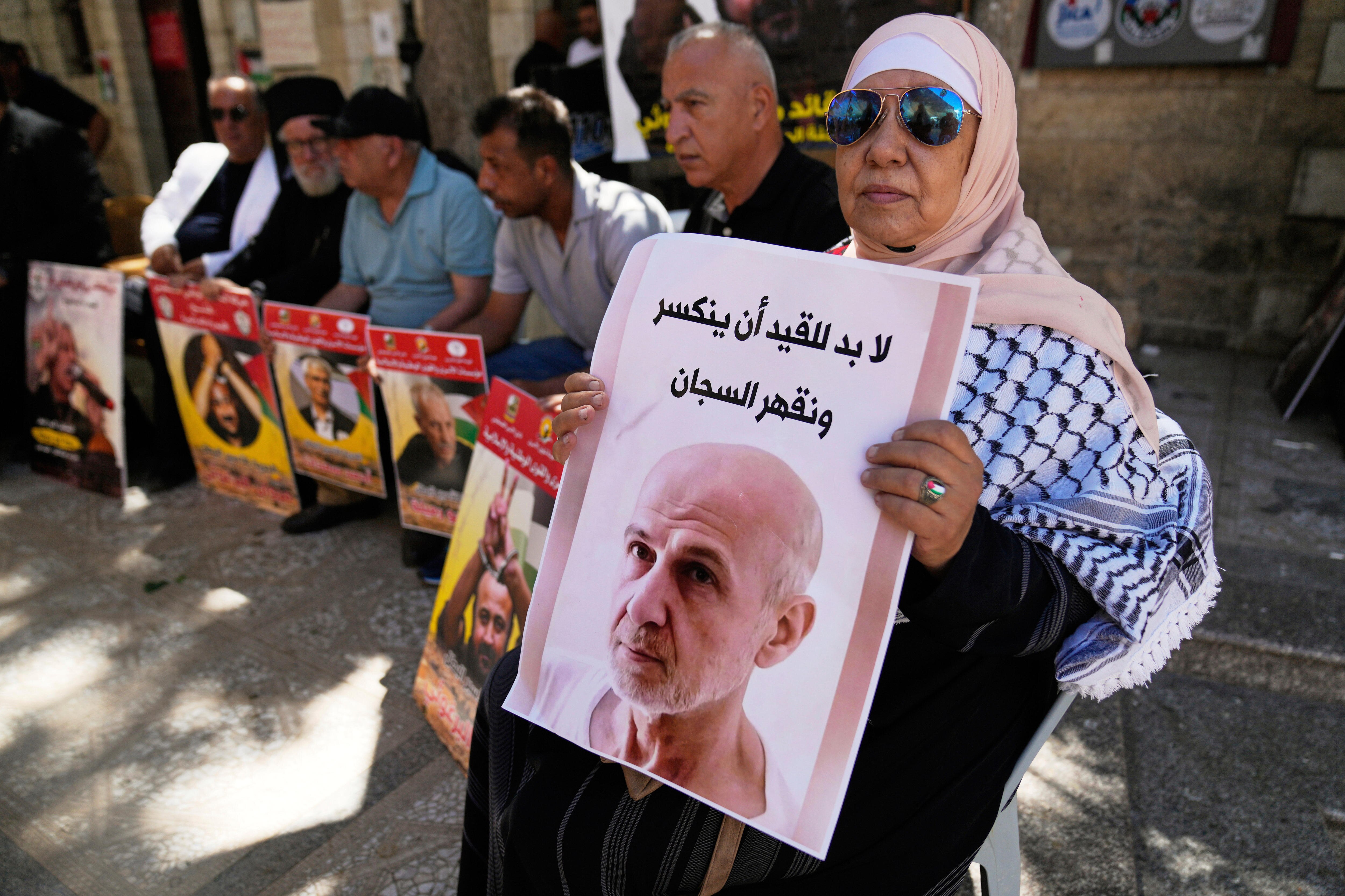 A woman in a hijab and sunglasses holds up a poster of Marwan Barghouti.