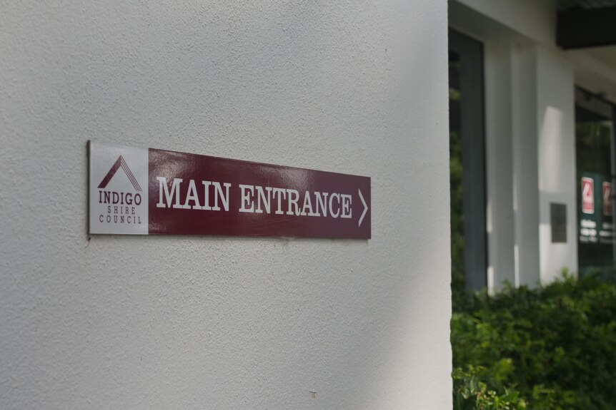 A maroon and white sign pointing to a library entrance