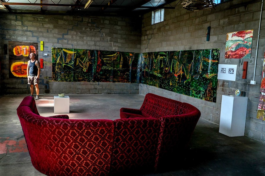 Man stands in industrial art space with beautiful red sofa.