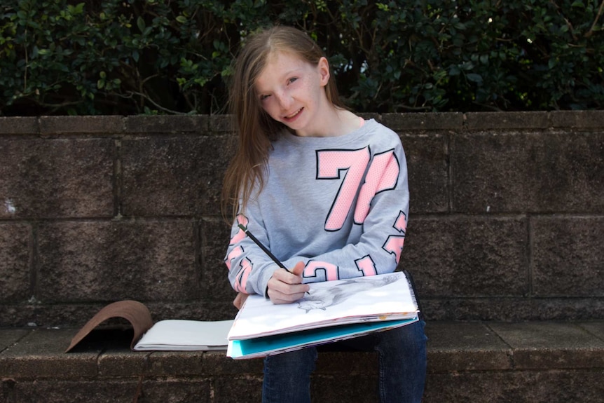 Stella Jackson sitting on a brick wall drawing