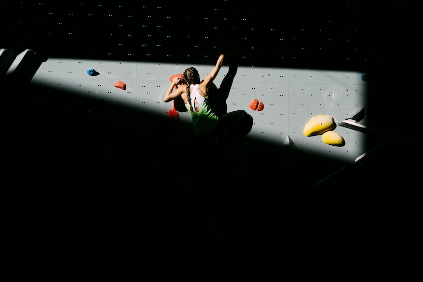 A shadowed picture of a young woman indoor rock climbing.
