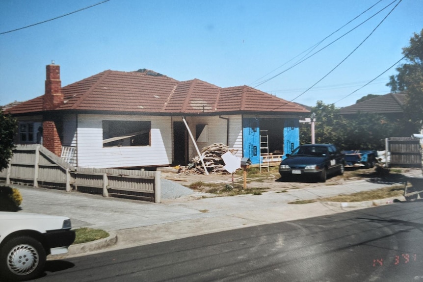 An old photo showing a white house with a brown tile roof and construction.