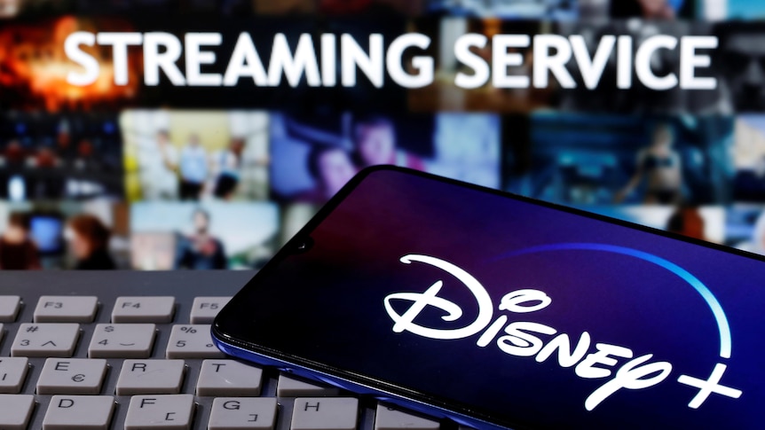 A smartphone with the Disney+ logo is seen on a keyboard in front of the words "Streaming Service".