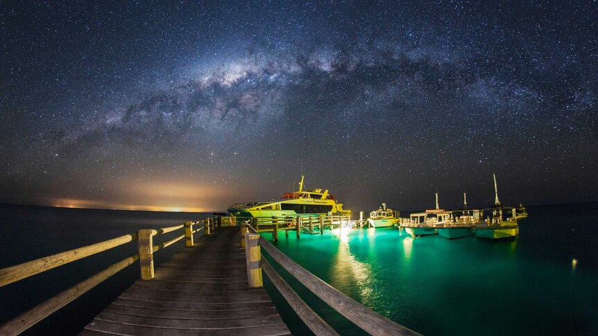 Boats tied up to jetty with clear, starry sky above