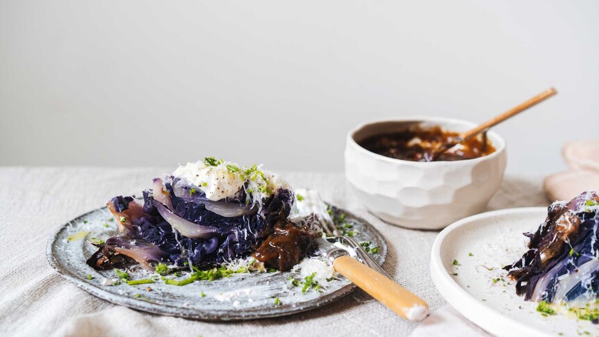 A plate of whole roasted red cabbage topped with sour cream, chives and onion gravy, a decadent vegetarian recipe.