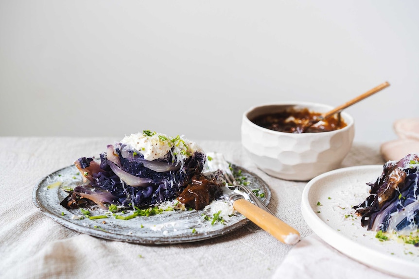 A plate of whole roasted red cabbage topped with sour cream, chives and onion gravy, a decadent vegetarian recipe.