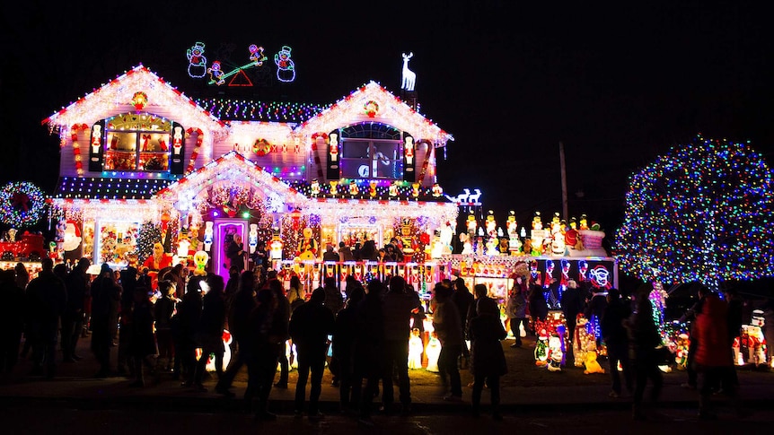 A crowd of people gathers outside a house elaborately decorated with Christmas lights.