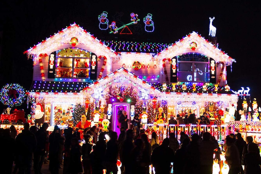 A crowd of people gathers outside a house elaborately decorated with Christmas lights.