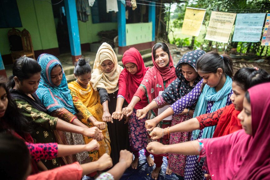 A group of young women standing in a circle putting their hands in the middle in Sylhet, Bangladesh.