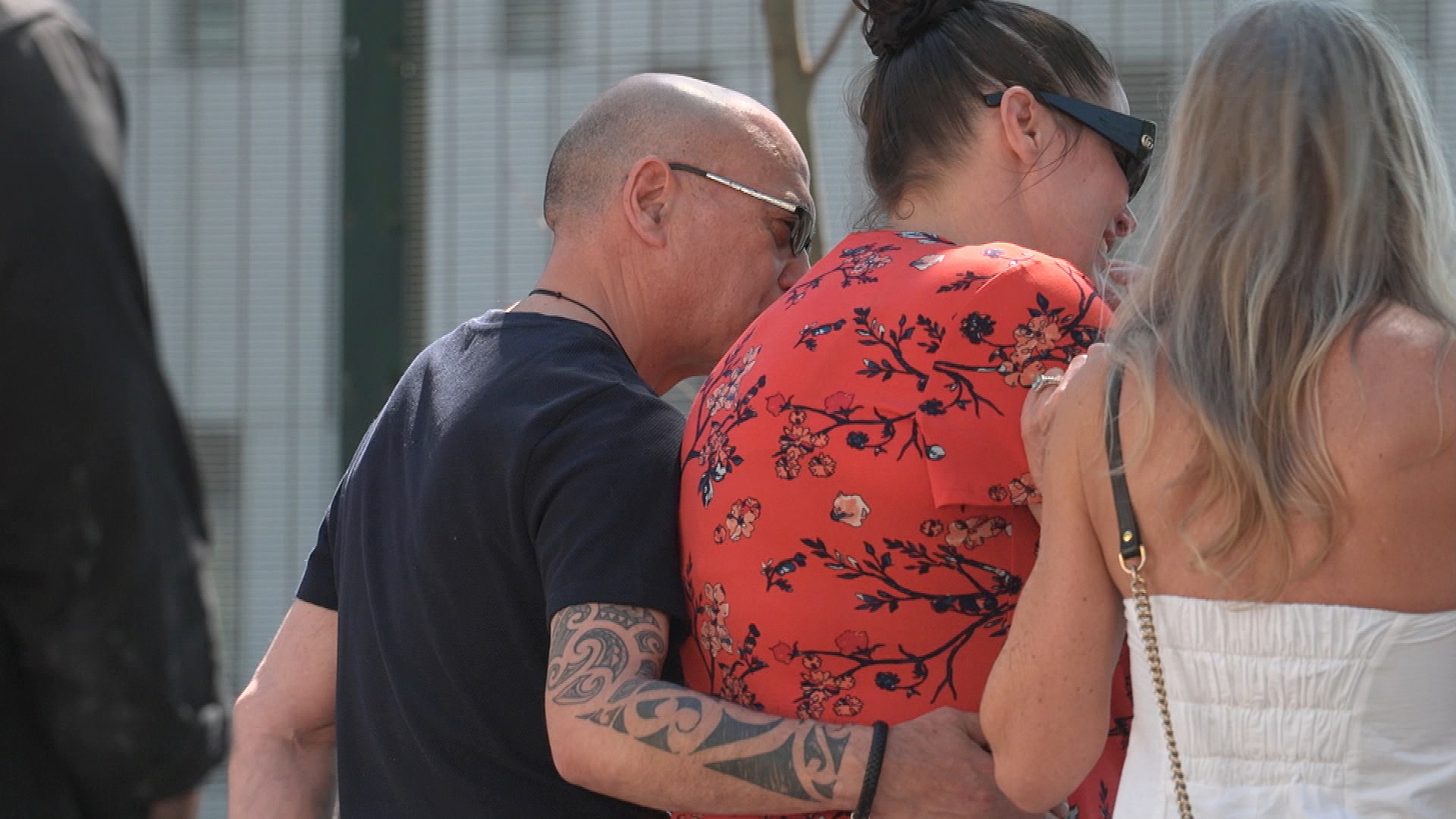 the back of a group of three people hugging and crying at the scene of a crash where an officer died