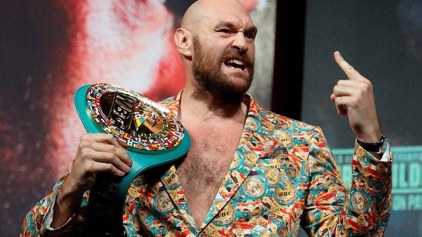 Tyson Fury snarls and points with his finger while holding a boxing belt