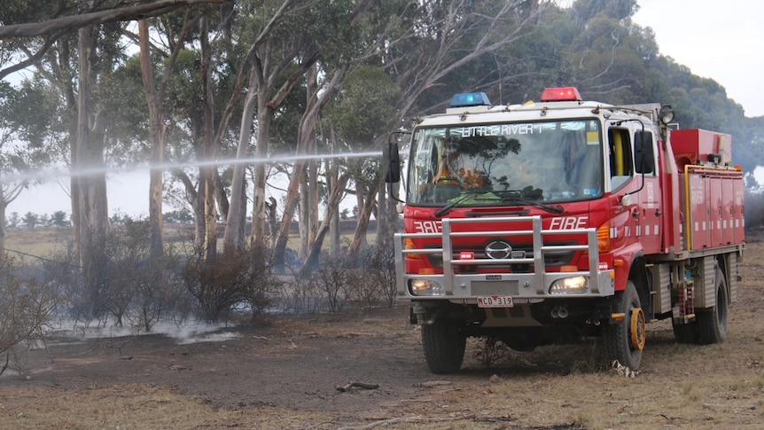 A red fire truck sprays water onto still smouldering scrub.