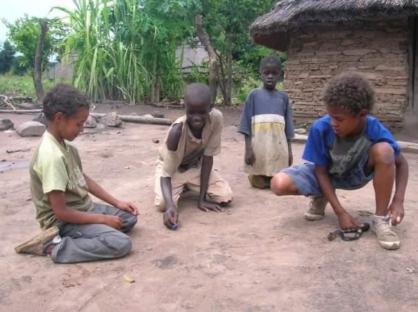 Four boys playing on dirt ground, one ties his shoelaces