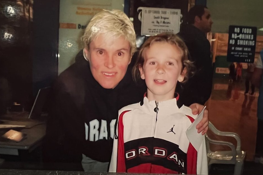 Steph Reid as a child, wearing a Michael Jordan tracksuit, smiles for a photo with Michelle Timms.