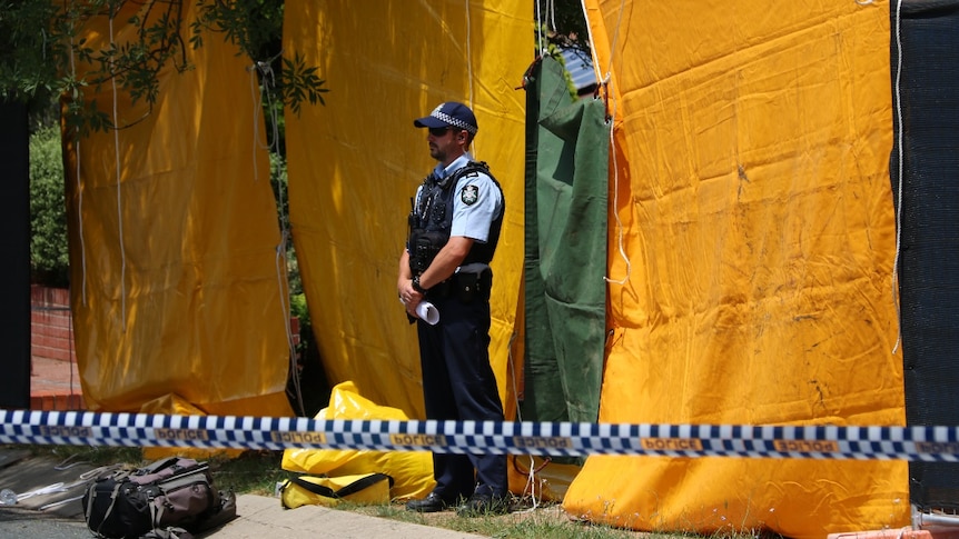 An officer stands in front of several tarps.