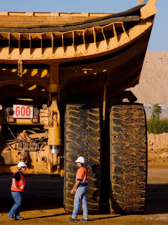 Two coal mining workers with the back of a large coal mining truck towering over them