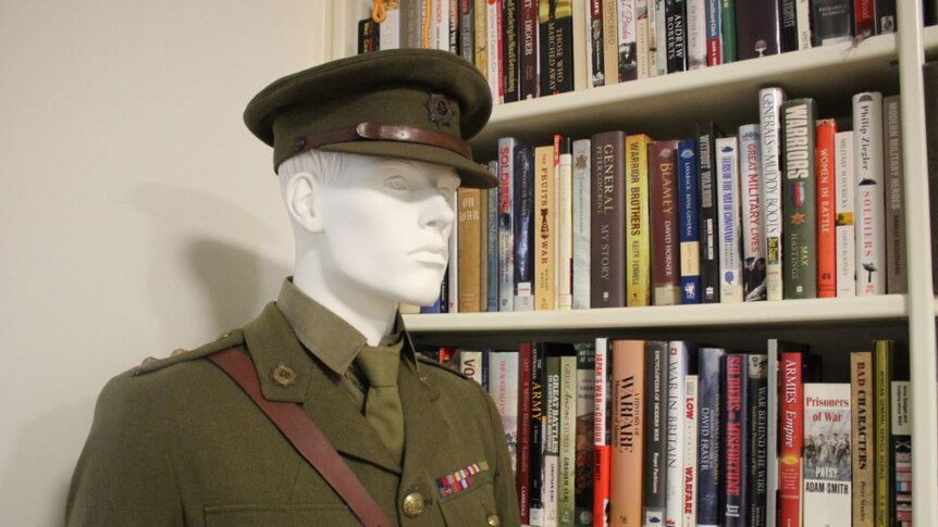 A mannequin wearing an army uniform stands next to a packed bookshelf.