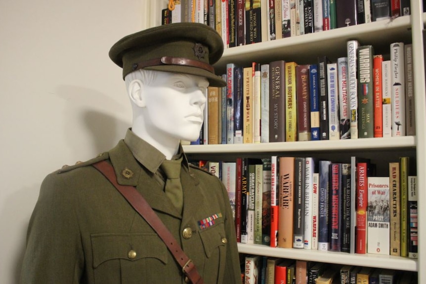 A mannequin wearing an army uniform stands next to a packed bookshelf.
