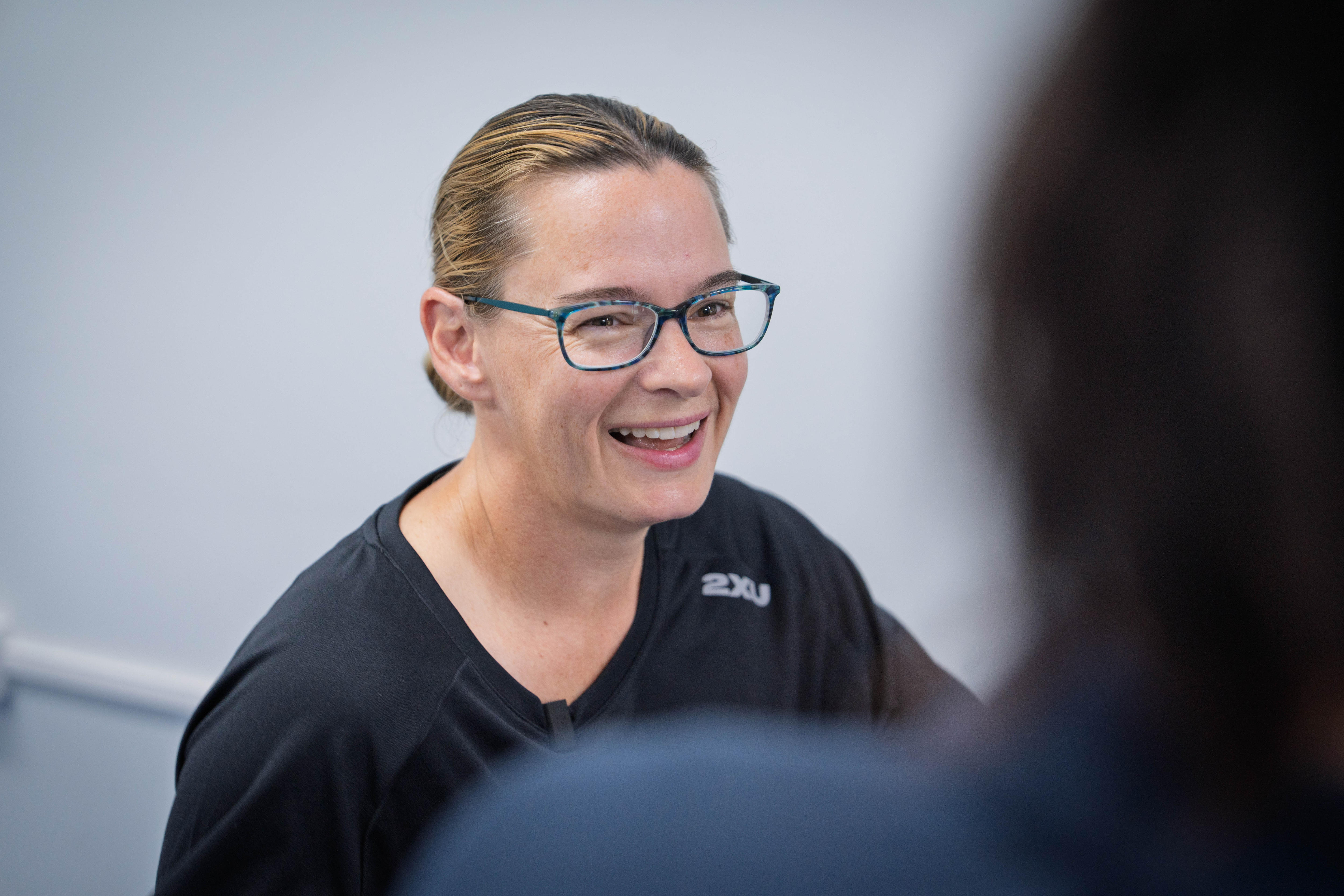 Una mujer sonríe ampliamente a otra persona fuera de cámara en una habitación.