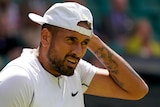 Nick Kyrgios holds his hat and looks up