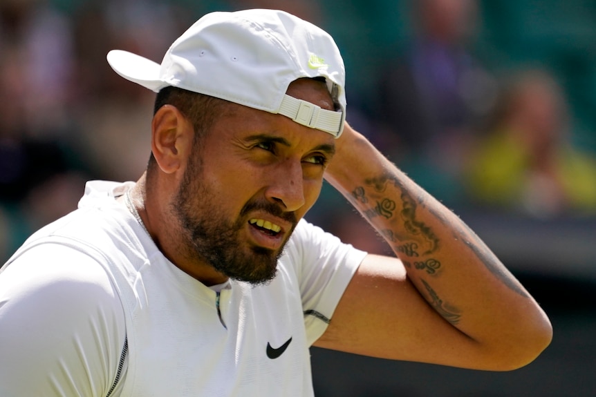 Nick Kyrgios holds his hat and looks up