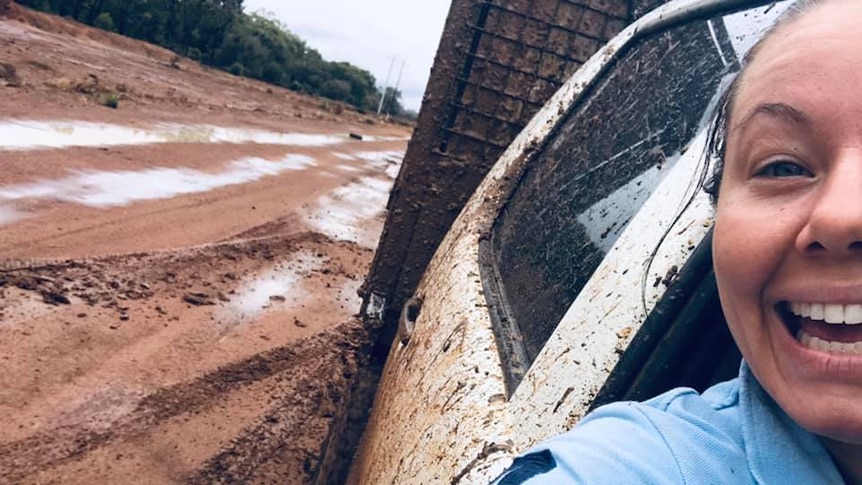 A smiling woman looking at the camera with mud on the back of her ute
