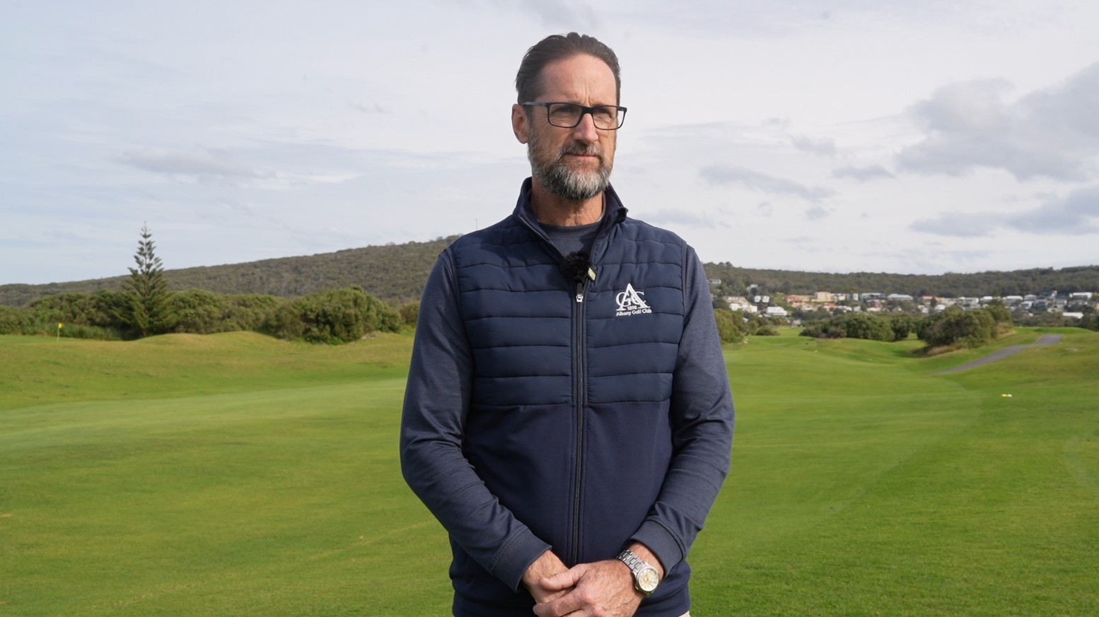 A man looks serious standing on a golf course.