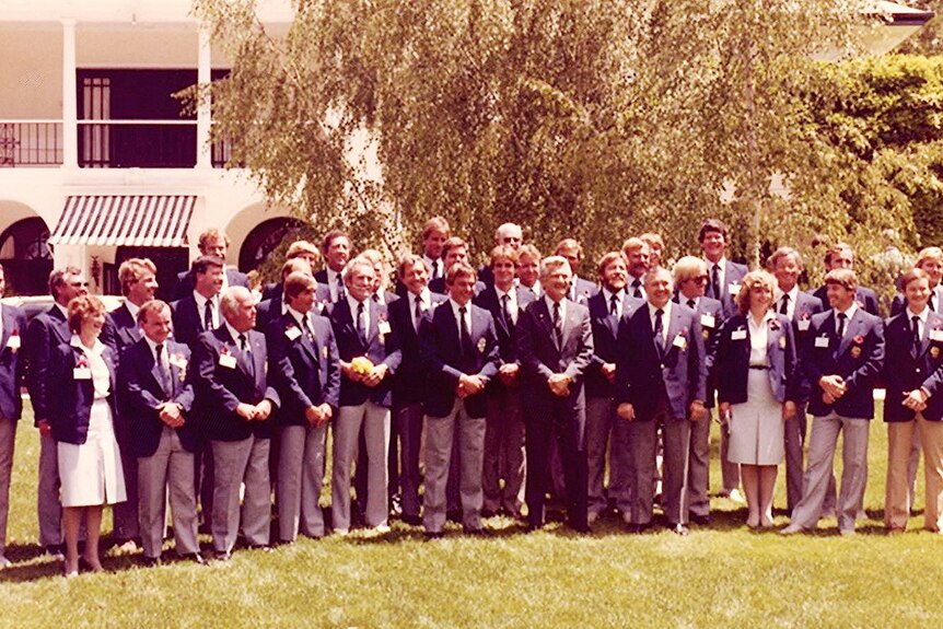 A group of smiling people in matching blazers stand on a lawn. Former prime minister Bob Hawke stands at the centre.