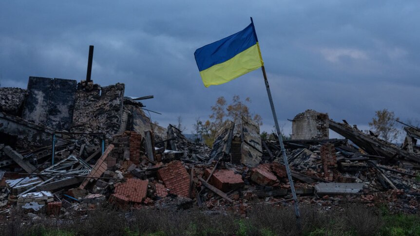A Ukrainian flag flies above the ruins of buildings