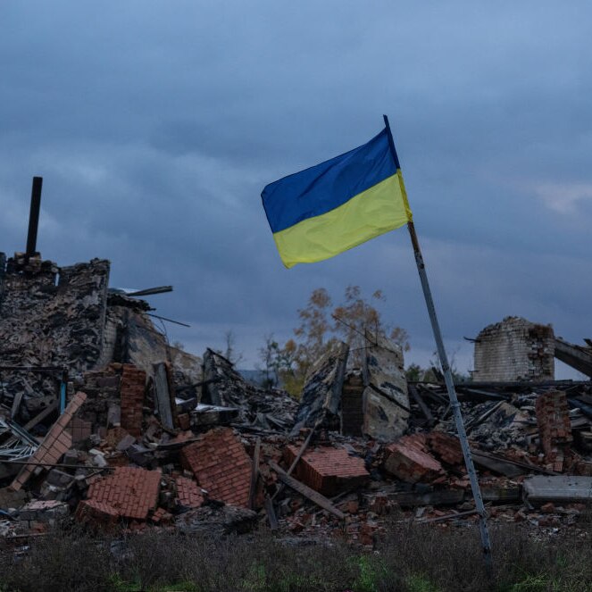 A Ukrainian flag flies above the ruins of buildings