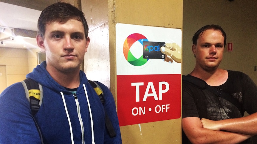 Two young men pose for the camera besides an Opal card post.