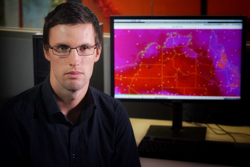 Forecaster sitting next to a computer showing a weather map.