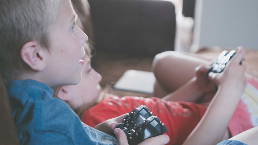 A young boy and a girl play video games while sitting on a couch, for a story about microtransactions.