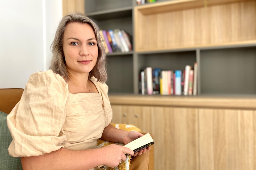 Woman sits in corporate clothing in front of a bookshelf with books, stagnant expression