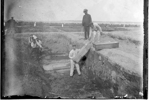 A black and white photo of men pulling coffins into a trench
