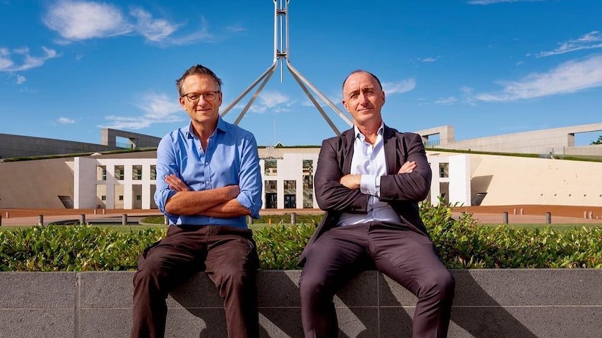 Michael Mosley and Ray Kelly sit on a wall with arms crossed with Parliament House in the background.