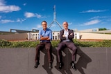 Michael Mosley and Ray Kelly sit on a wall with arms crossed with Parliament House in the background.