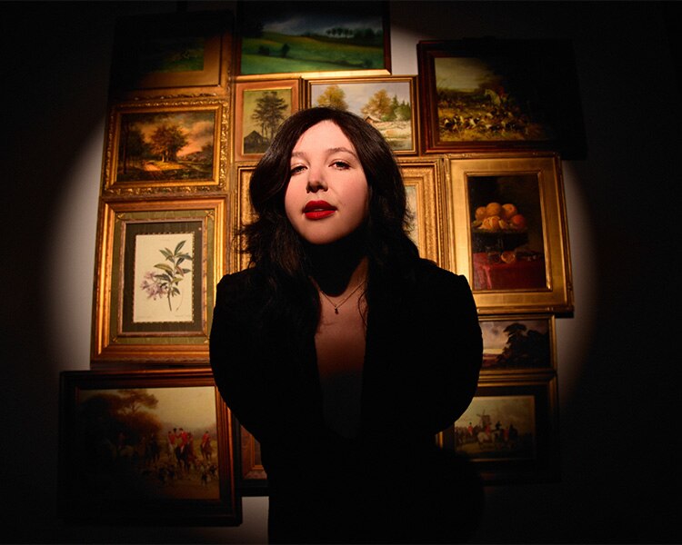 Lucy Dacus album cover, she stands in front of a wall of paintings while looking at the camera