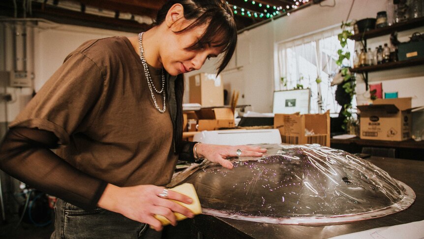Woman sanding clear plastic in the shape of a shield.