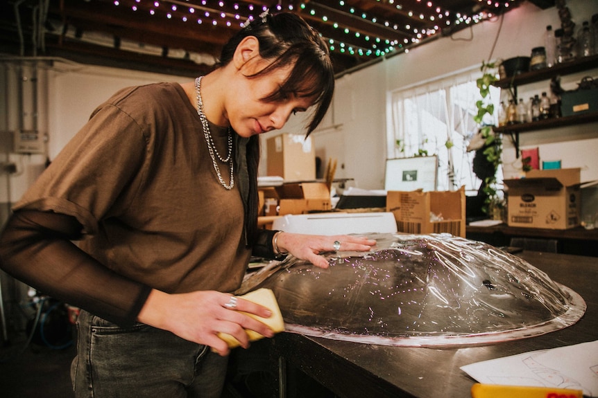 Woman sanding clear plastic in the shape of a shield.