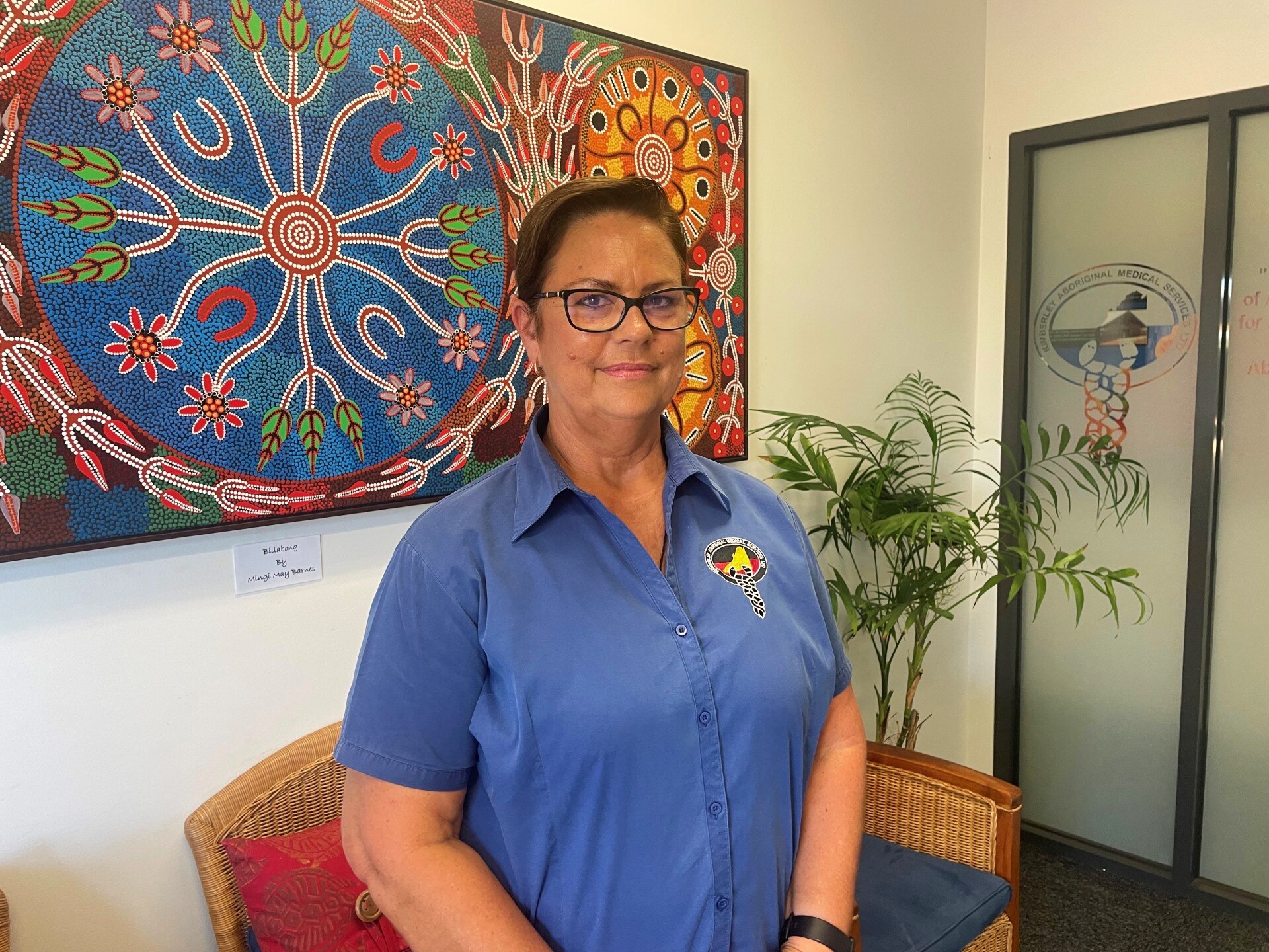 Lorraine Anderson stands and smiles in front of a painting.