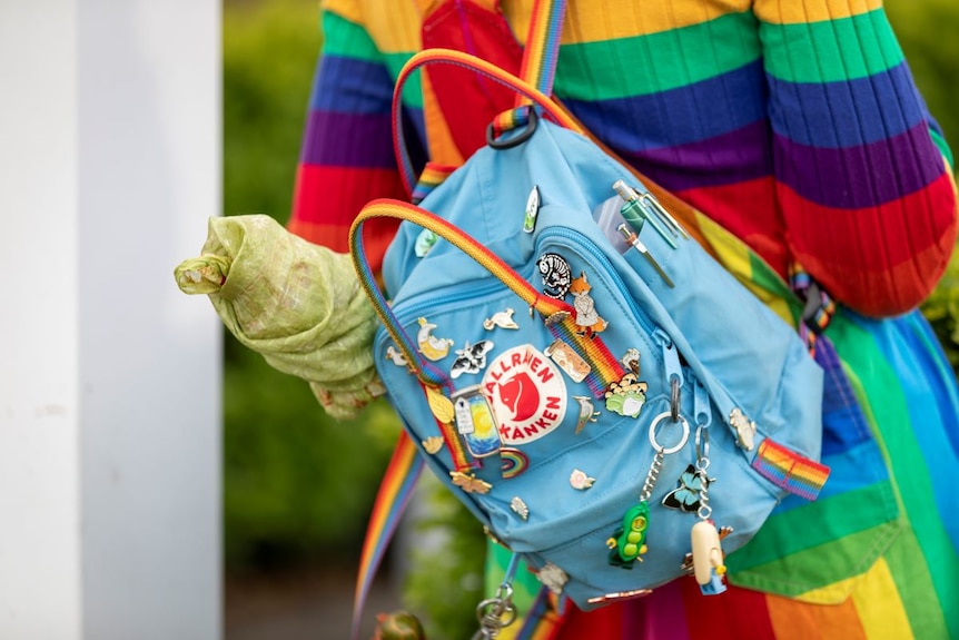 A pale blue backpack with rainbow straps and coloured badges and keyrings.