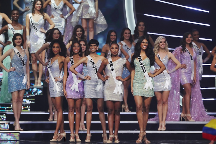 Multiple women stand on stage competing in Miss Universe pageant.