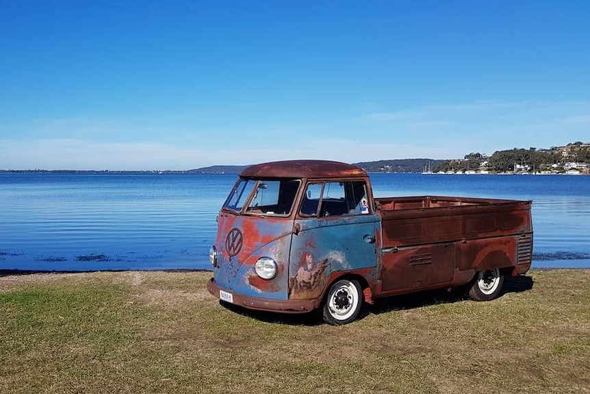Old restored Kombi ute parked beside a lake on a sunny day
