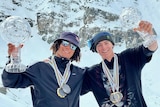 Two snowboarders with medals around their necks smile as they hold crystal globe trophies after the final event of a season.  