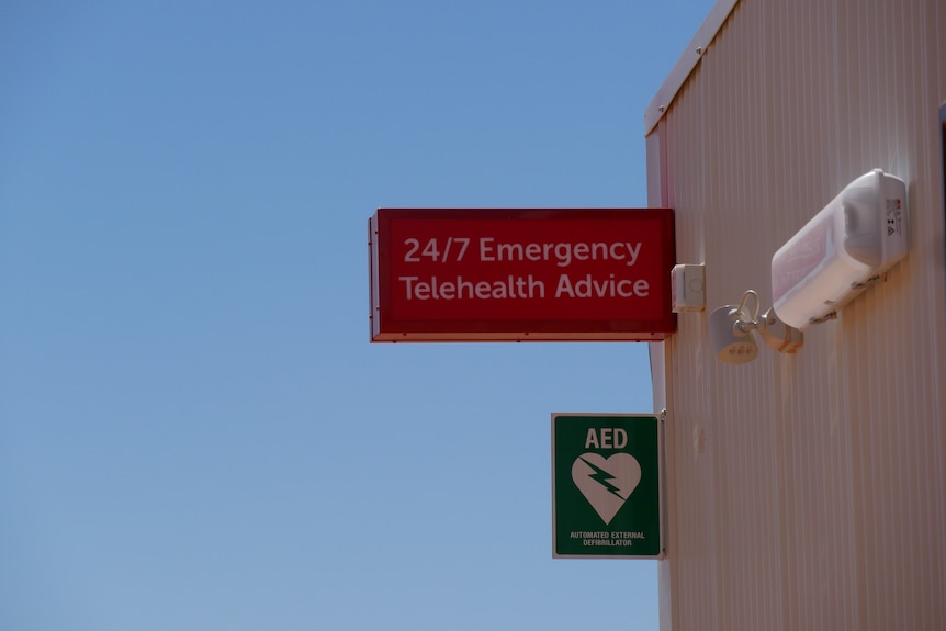 A red sign on the outside of a building reading '24/7 Emergency Telehealth Advice'