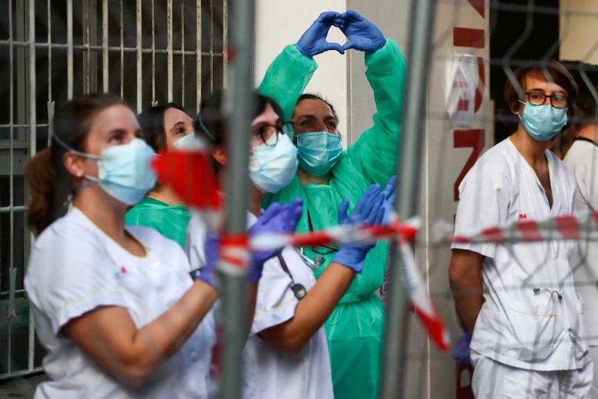 A medical worker makes a heart shape with her hands while looking up to the sky